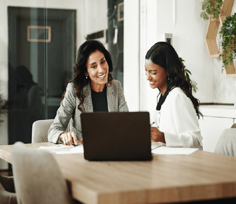 Two women smiling at a laptop screen.